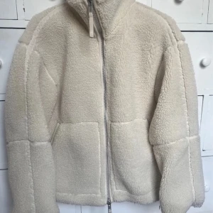 Beige teddyjacka med dragkedja hm  - Mysig beige teddyjacka i mycket bra skick. Perfekt för höst och vinter med sin varma och fluffiga design. Jackan har en dragkedja framtill och långa ärmar. Den är både stilren och bekväm, idealisk för kyliga dagar. Dragkedjans söm har lossnat pyttelite men de är ingenting som påverkar alls. Storlek xs men passar även M 