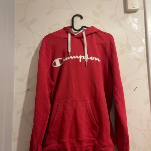 Röd hoodie från Champion - Säljer en snygg röd hoodie från Champion i bra skick. Den har en klassisk känguruficka och justerbar huva med vita snören. Perfekt för höst och vinter, både mysig och stilren. Passar lika bra till vardags som till träning. 🏆