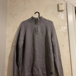 Grå stickad tröja med dragkedja från Bondelid - Säljer en snygg grå stickad tröja med halv dragkedja från Bondelid. Perfekt för kyliga dagar med sitt mysiga material och stilrena design. Tröjan har långa ärmar och ribbade detaljer vid krage, ärmslut och nederkant. Passar både till vardags och lite finare tillfällen.