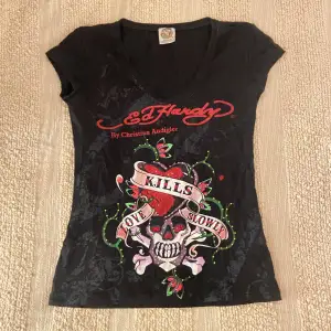 Säljer en svart Ed Hardy t-shirt med rhinestones och ett coolt tryck av en dödskalle och hjärta med texten ”Love Kills Slowly”. T-shirten har en v-ringad hals och korta ärmar. Perfekt för en edgy look! Skulle säga att den är lite mindre i storleken men är stretchig! 🖤DM vid frågor osv! ❗️pris kan diskuteras vid snabb affär❗️