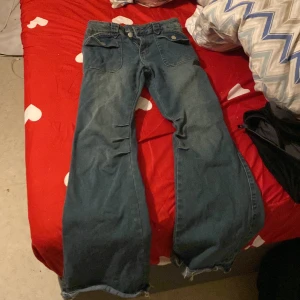 Blå jeans med vida ben - Säljer ett par blå jeans i bra skick med vida ben och hög midja. De har snygga fickdetaljer med knappar framtill och en klassisk jeanslook. Perfekta för en avslappnad stil eller en dag på stan. Passar bra till både sneakers och boots!