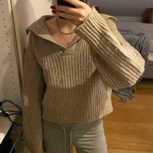 Beige stickad tröja - Säljer en supermysig beige stickad tröja med en djup v-ringning och krage. Den är croppad och har långa ärmar, perfekt för höst och vinter. Tröjan är i bra skick och passar perfekt till både jeans och kjol. Perfekt för en avslappnad stil! 🍂