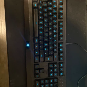 Gamingtangentbord med RGB-belysning - Säljer ett gamingtangentbord med justerbar RGB-belysning. Tangentbordet har en robust design med svarta tangenter och möjlighet att ändra färg på belysningen. Perfekt för gaming eller arbete i mörka miljöer. Ansluts via USB.