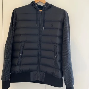 Unik Ralph lauren cardigan ‼️ - Säljer en snygg svart cardigan från Ralph Lauren i storlek M (Passar S). Jackan har ett coolt rutigt mönster på ärmarna och huvan, samt en dragkedja framtill. Perfekt för höst och vinter med sin quiltade design. Den är helt ny och redo för nya äventyr! Kan mötas upp i Stockholm 