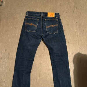 Mörkblå jeans från Nudie - Säljer ett par snygga mörkblå jeans från Nudie i storlek W29/L29. Det står att de är 34 i längd men tyvär så har ägaren sytt upp de. De sitter lite tajt så rekommenderar att om ni är mindre i midjan så borde ni absolut köpa