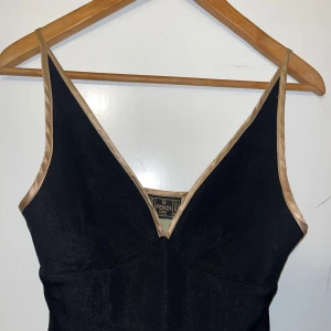 Vintage topp Fendi med blommigt mönster - Snygg svart topp från Fendi med en v-ringad design och blommigt mönster i rosa och blått på insidan. Toppen har en elegant passform och är perfekt för festliga tillfällen. Den har en dragkedja på sidan för enkel påklädning.