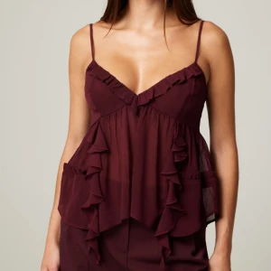 Vinröd ärmlös topp med volanger - Säljer en superfin vinröd topp med smala axelband och volangdetaljer från bikbok. Perfekt för sommaren eller en festlig kväll. Helt ny med prislapp kvar.