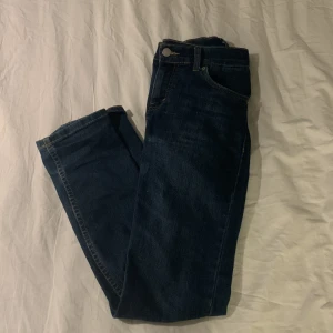 Mörkblå jeansbyxor - Säljer ett par klassiska mörkblå jeansbyxor i mycket bra skick. De har en snygg straight passform och är perfekta för både vardag och fest. Byxorna har en traditionell femficksdesign och stängs med dragkedja och knapp. Perfekta för höst och vår!