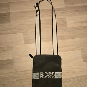 Svart axelväska från Hugo Boss - Säljer min Hugo boss väska för jag använder den inte mer.                                                     Använt den typ 5 gånger så den e i perfekt skick.                                                                   Köpte den för 1300kr.                                                 Säljer för 500kr men kan diskutera pris eller byta väskan mot något. KAN HÄMTAS
