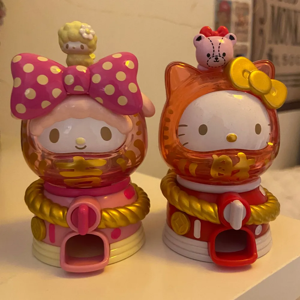 Två supersöta figurer från Sanrio! En Hello Kitty i orange med gul rosett och en Sweet Piano i rosa med prickig rosett. Båda har små figurer på huvudet och är dekorerade med gulddetaljer. Perfekta för samlare eller som dekoration i rummet!. Accessoarer.