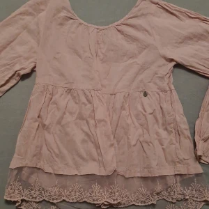 Ljusrosa blus med spetsdetaljer - Detta gör ont att sälja då denna är och har varit min favorit tröja sen dag ett jag fick den och nu är den alldeles för liten för mig och därmed måste jag sälja vidare den så den fortfarande kan användas. Jag vet inte vart den är ifrån tyvärr då jag fick den för några år sedan och den är FÖR sparsamt använt (som ny), så jag säljer denna super söta ljusrosa blusen med vacker spetsdetalj längst ner. Blusen har en liten silverfärgad berlock med en fjäril på framsidan. Perfekt för vår och sommar! 🌸