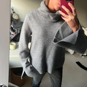 Grå stickad polotröja - Mysig grå stickad polotröja med en stor, bekväm krage. Perfekt för kyliga dagar med sin avslappnade passform och långa ärmar. Ribbstickade detaljer vid ärmslut och nederkant ger en extra touch. Perfekt för både vardag och mysiga hemmakvällar.