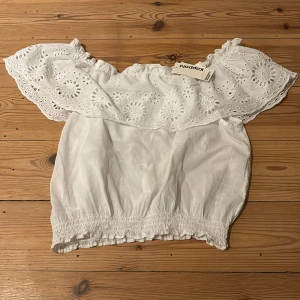 Vit offshoulder topp från Kappahl  - Säljer en superfin vit offshoulder topp från Kappahl . Den har vackra spetsdetaljer och en elastisk nederkant för en bekväm passform. Perfekt för sommarens alla fester eller en dag på stan. Helt ny med tag kvar!