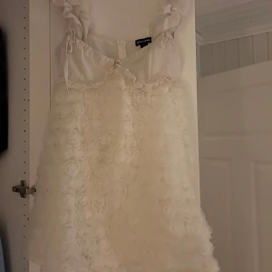 Vit klänning från PrettyLittleThing - Superfin vit klänning från PrettyLittleThing med ett unikt blommigt mönster. Den är ärmlös och har en söt volangdetalj vid axlarna. Perfekt för studenten eller sommarens fester . Klänningen är i nytt skick och redo att bäras för att göra ett statement! 🌸dock så kom den med en spricka i innertyget, inget man tänker på när man har på sig den då det inte syns! Aldrig andvänt innan!