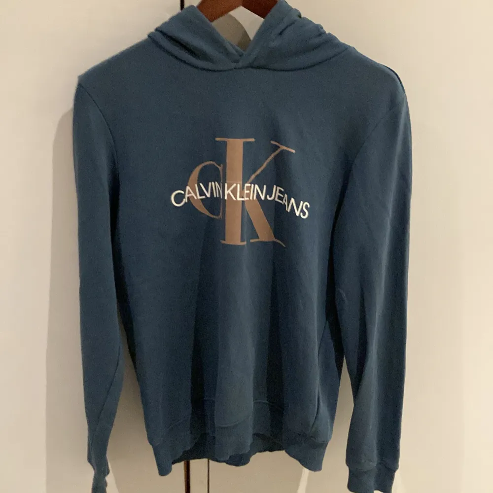 Säljer en snygg blå hoodie från Calvin Klein Jeans. Den har en stor logga på framsidan och är i mycket bra skick. Perfekt för höst och vår, med långa ärmar och en skön luva. Passar både till vardags och chillkvällar. . Tröjor & Koftor.