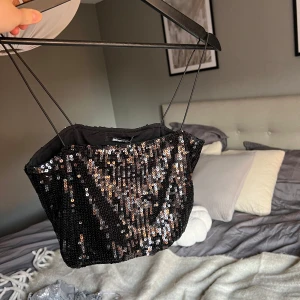 Svart paljettprydd tubtopp från Gina Tricot - Snygg svart tubtopp från Gina Tricot, täckt med glittrande paljetter. Perfekt för festliga tillfällen! Den har tunna axelband och en tight passform som framhäver figuren. Toppen är i nytt skick med etikett kvar.