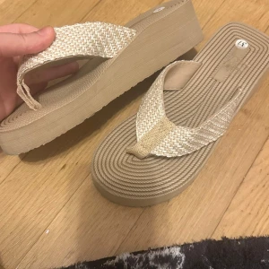 Beige sandaler med flätad rem - Säljer ett par snygga beige sandaler med flätad rem. Perfekta för sommaren med en bekväm sula och stilren design. De är i storlek 37 och passar perfekt för en avslappnad dag på stranden eller en promenad i solen.