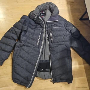 Svart pufferjacka från Peak Performance - Säljer en svart pufferjacka från Peak Performance i mycket bra skick. Jackan har en hög krage och flera praktiska fickor med dragkedjor. Perfekt för kalla vinterdagar och håller dig varm och bekväm. Passar både till vardags och utomhusaktiviteter.