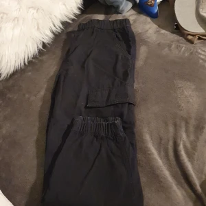 Svarta cargopants med elastisk midja - Säljer ett par svarta cargopants i ok skick.      . De har en elastisk midja för extra komfort och flera praktiska fickor.. Perfekta för en avslappnad stil eller vardagsäventyr. 