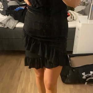 Svart kjol med volangdetaljer - Säljer en superfin svart kjol med volangdetaljer. Perfekt för fest eller en utekväll! Kjolen är kort och har en tight passform som framhäver figuren. Den är gjord i ett mjukt och bekvämt material, vilket gör den både snygg och skön att bära. 