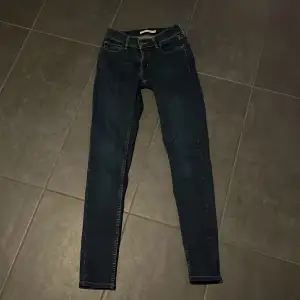 Säljer ett par mörkblå super skinny jeans i storlek 26. De är i bra skick och perfekta för både vardag och fest. Passformen är tight och de har en klassisk femficksdesign med dragkedja och knapp. Perfekta för dig som gillar en stilren look!