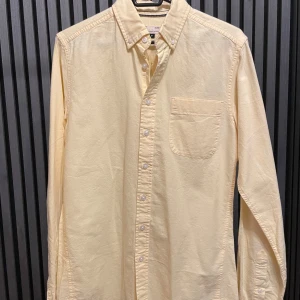 Gul skjorta från Dressmann - Säljer en stilren gul skjorta från Dressmann i storlek S. Skjortan är slim fit och tillverkad av 100% bomull, vilket gör den både bekväm och andningsbar. Den har långa ärmar och knappar framtill samt en bröstficka. Perfekt för både vardag och festliga tillfällen!