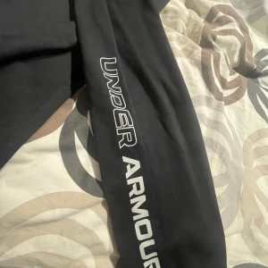 Svarta träningsbyxor från Under Armour - Säljer ett par svarta träningsbyxor från Under Armour i storlek 147-158. Byxorna har en elastisk midja och är perfekta för träning. De är i bra skick och har en snygg logga längs benet. Perfekta för gymmet eller löprundan!