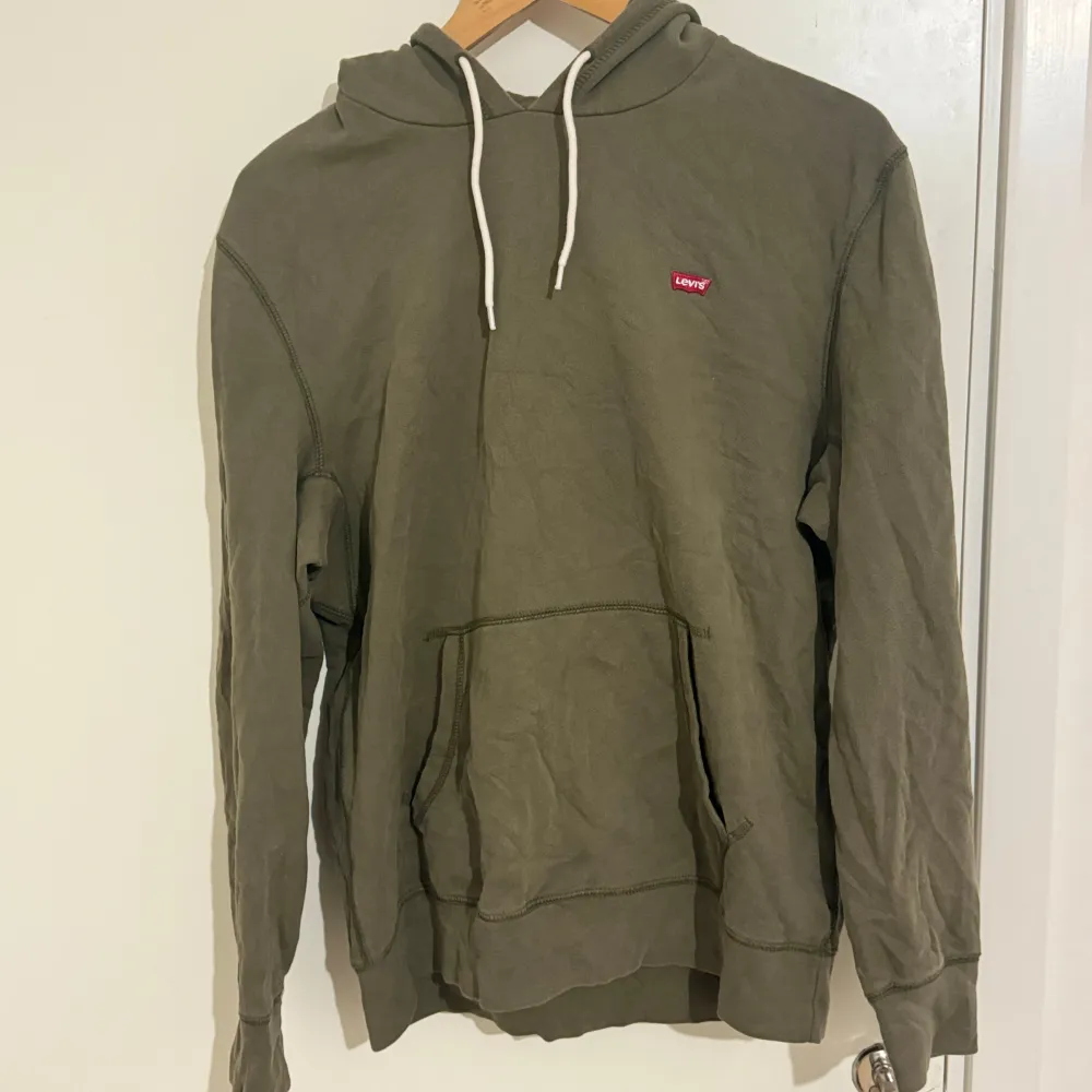 Säljer en snygg olivgrön hoodie från Levi's i storlek S. Den har en klassisk design med en känguruficka och justerbar huva med vita snören. Perfekt för en avslappnad stil och passar bra till både jeans och joggers. Använd men i bra skick!. Tröjor & Koftor.