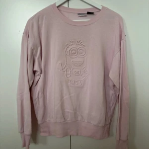 Rosa sweatshirt med Minion-motiv - Säljer en supermjuk rosa sweatshirt med Minion-motiv på framsidan. Tröjan har långa ärmar och i mycket bra skick.