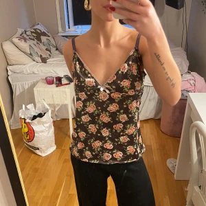 Blommig linne i satin - Säljer ett supercharmigt blommigt linne i satin med smala axelband. Linnet har en mörk bas med vackra rosor i rosa och grönt. Det är i mycket bra skick. 🌺