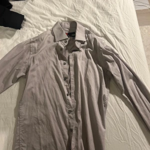 Beige skjorta från Dressmann - Säljer en stilren beige skjorta från Dressmann i storlek S. Skjortan har en slim fit passform och är perfekt för både vardag och fest. Den är långärmad med knappar hela vägen ner. Materialet känns mjukt och bekvämt. Perfekt för höst och vår!