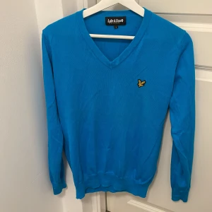 Blå tröja från Lyle & Scott - Säljer en snygg blå tröja från Lyle & Scott i storlek S. Den har en v-ringad design och ett broderat emblem på bröstet. Perfekt för både vardag och fest! 💙