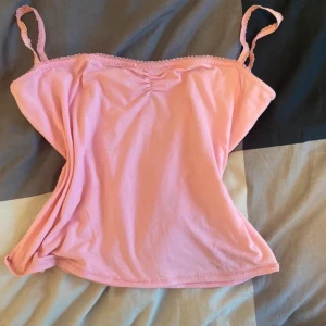 Rosa linne med smala axelband - Säljer ett sött rosa linne med smala axelband och rynkdetalj framtill. Perfekt för sommardagar eller som ett lager under en tröja. Linnet är i bra skick och har en mjuk och bekväm passform.