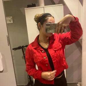 Röd croppad jacka - Säljer en snygg röd croppad jacka med knappar framtill. Perfekt för att ge din outfit en färgklick! Jackan har långa ärmar och en cool, avslappnad stil. Passar perfekt till både vardag och fest.