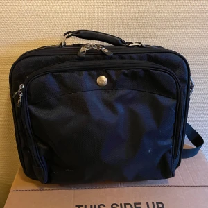 Svart datorväska från Dell - Säljer en svart datorväska från Dell i bra skick. Väskan har flera fack med dragkedja och en bekväm axelrem. Perfekt för att bära din laptop och tillbehör säkert och stiligt. Passar både för jobb och studier.