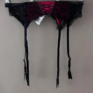 Svart och röd spetsstrumpebandshållare - Säljer en elegant svart och röd strumpebandshållare från Censored i storlek EU 36. Den har vacker spetsdetalj och justerbara band för perfekt passform. 