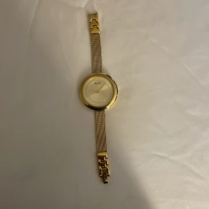 Guldfärgad klocka från Boss - Säljer en elegant guldfärgad klocka från Boss. Den har en stilren design med ett mesh-armband och en rund urtavla. Perfekt för både vardag och fest. Klockan är i fint skick och ger en lyxig känsla.
