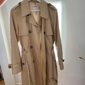 Beige trenchcoat från Esprit - Säljer en klassisk beige trenchcoat från Esprit i mycket bra skick. Den har långa ärmar och knappar framtill samt ett bälte i midjan för en snygg passform. Perfekt för höst och vår! 🌟