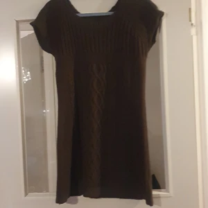Brun stickad klänning - Mysig brun stickad klänning med korta ärmar och ett snyggt flätmönster framtill. Perfekt för höst och vinter, den är både varm och stilren. Passar bra till både vardag och festliga tillfällen.