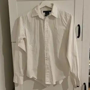 Säljer en stilren vit skjorta från Ralph Lauren i slim fit. Skjortan är i mycket bra skick och har långa ärmar samt knappar framtill. Den är tillverkad i 95% bomull och 5% elastan, vilket ger en skön passform. Perfekt för både vardag och fest! 🕺