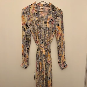 Mönstrad långklänning med bälte - Säljer en superfin långklänning med ett färgglatt mönster. Klänningen har långa ärmar och ett knytbälte i midjan för en snygg passform. Perfekt för både vår och sommar men även höst med boots! 🌸