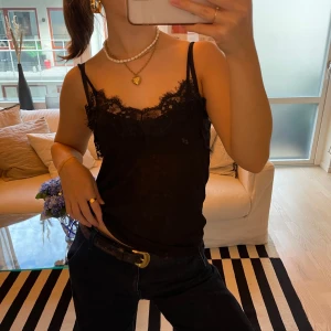 Svart linne med spetsdetaljer - Säljer ett svart linne med tunna axelband och vacker spetsdetalj vid halsringningen!