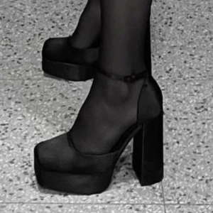 Svarta platåpumps med klack - Säljer ett par snygga svarta platåpumps i mycket bra skick. De har en hög blockklack och en elegant rem runt ankeln. Perfekta för fest eller en utekväll när du vill sticka ut lite extra. Materialet ser ut att vara syntetiskt och de har en modern, stilren design. Ord pris 1000kr 