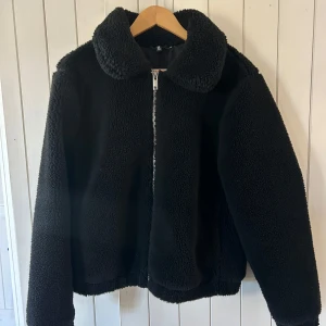 Svart teddyjacka från HM - Mysig svart teddyjacka från HM i mycket bra skick. Jackan har en dragkedja framtill och är perfekt för kyliga höst- och vinterdagar. Den är långärmad och har en klassisk krage som ger en stilren look.
