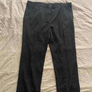 Svarta kostymbyxor - Säljer ett par stilrena svarta kostymbyxor i slim fit. De har en dragkedja och knapp framtill samt diskreta fickor med dragkedja. Perfekta för både formella tillfällen och vardagsbruk. Materialet känns bekvämt och passar bra till höst och vår.