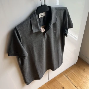  Burberry pikétröja  - Säljer en snygg grå pikétröja från Burberry i helt nytt skick. Den har en klassisk krage och korta ärmar, perfekt för både vardag och lite finare tillfällen. Passar perfekt för dig som gillar stilrena plagg med hög kvalitet. Mvh ItsForFits 🌟