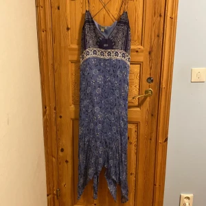 Blå långklänning från Lucky Brand - Säljer en vacker blå långklänning från Lucky Brand. Klänningen har ett blommigt mönster och smala axelband som korsas i ryggen. Den är perfekt för sommarens fester med sin luftiga och bekväma passform.