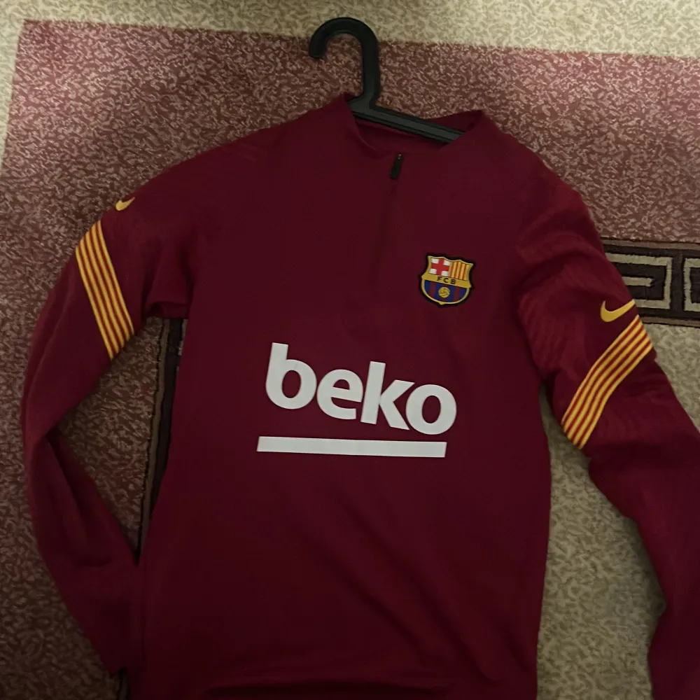 Säljer en vinröd långärmad Barcelona fotbollströja från Nike i Dri-FIT material. Tröjan har gula detaljer på ärmarna och klubbens emblem på bröstet. Perfekt för fans som vill visa sitt stöd med stil! 🏆 Skick 8/10 pris kan diskuteras. Extremt sällsynt tröja.. Hoodies.