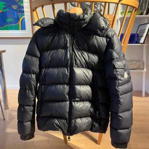 Säljer en snygg svart pufferjacka från Moncler i mycket bra skick. Jackan har en dragkedja framtill och en praktisk ficka med knapp på ärmen. Perfekt för kalla vinterdagar med sin varma och quiltade design. Passar både till vardags och lite finare tillfällen. 🖤Skriv i dm och ni vill ha fler bilder och diskutera pris! 