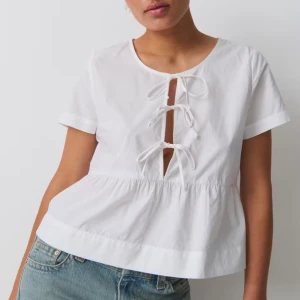 Vit blus med knytning - Säljer en söt vit blus med korta ärmar och knytning framtill. Perfekt för sommardagar eller en avslappnad vårlook. Blusen har en luftig passform och är gjord i ett lätt bomullsmaterial.